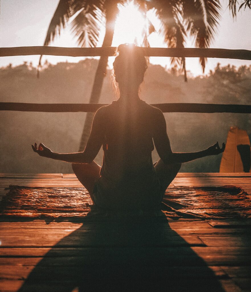 A woman sitting on a deck in a tropical paradise, meditating in the Lotus position bathed in sunlight